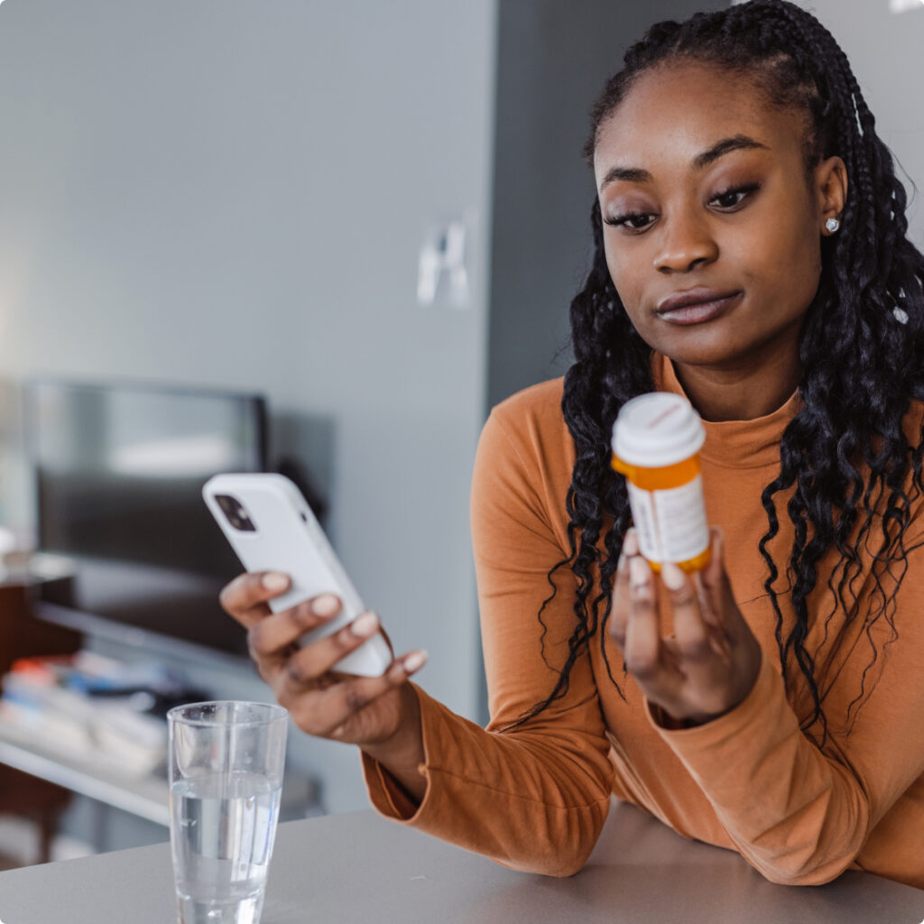 Woman holding medication on on hand and a phone on the other